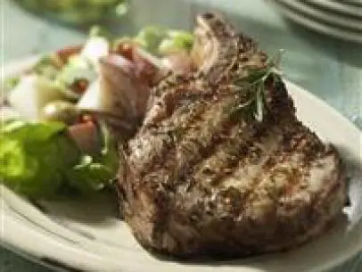 A Grilled Pork Chop Sprinkled With Spices on a Plate Beside a Salad