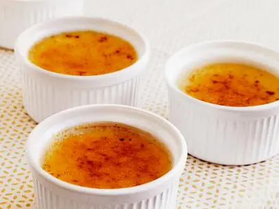 Desserts in three small white dishes on a patterned tablecloth