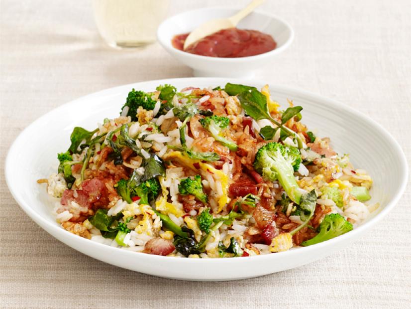 A fried rice, vegetables and bacon mixture in a white and gray bowl on a tan table setting