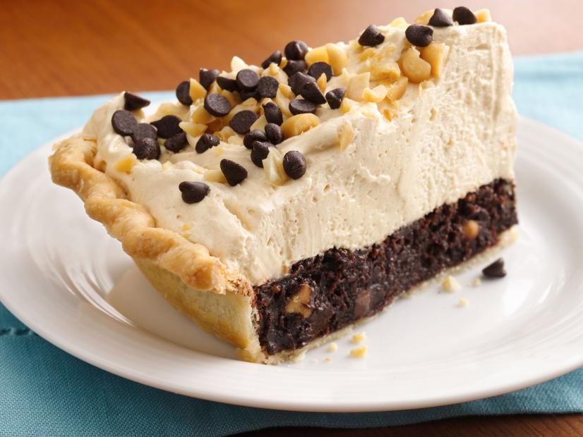 A slice of pie made of a brownie, whipped topping and topped with nuts and chocolate chips