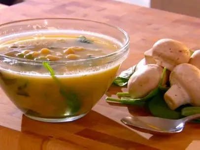 Soup in a glass bowl beside mushrooms and bay leaves