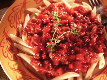 A meaty tomato sauce atop pasta in an orange dish with red designs