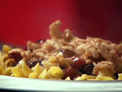 A steak and bacon mixture on a bed of pasta against a red background