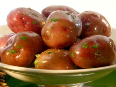 Boiled red potatoes have been drizzled with melted butter and sprinkled with chopped parsley leaves.