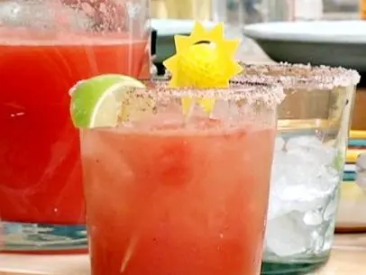A glass of watermelon margarita is served with a garnish of lime and a sun made on a toothpick.
