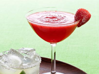 A red margarita garnished with a frozen strawberry in a long stemmed glass placed on a round wooden tray