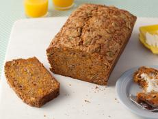 A loaf of Brown Pumpkin Bread with one slice removed that is placed on a plain white surface