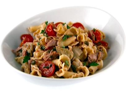 Campanelle pasta mixed with tomatoes, tuna, capers and artichoke hearts in a simple white boat shaped bowl