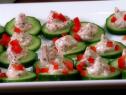 Several slices of cucumber with a goat cheese topping and chopped red bell peppers on a simple white platter