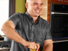 Michael Symon smiling as he twists a lid on a jar of sliced tomatoes