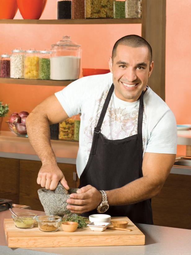 Next Food Network Star Finalist Herb Mesa smiling while wearing a t-shirt and black apron
