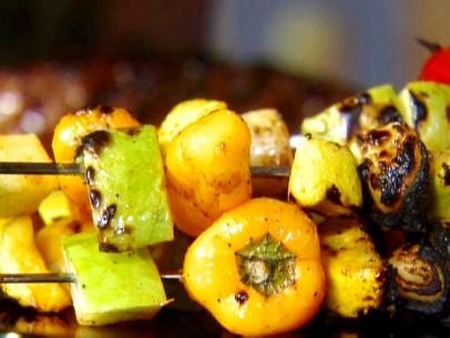Summer veggie kebabs are stacked on metal skewers with bell peppers, summer squash, chayote squash, and shallots.