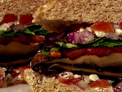 A close up of a grilled portobello burger with a vegetable salsa of plum tomatoes, red onions, feta cheese, charred red bell peppers, fresh oregano, 