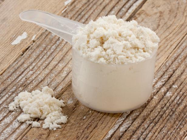 a scoop of whey protein isolate powder on a grunge wooden table background