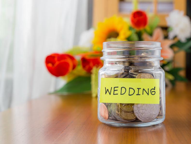 Many world coins in a money jar with wedding label on jar, beautiful flowers on background