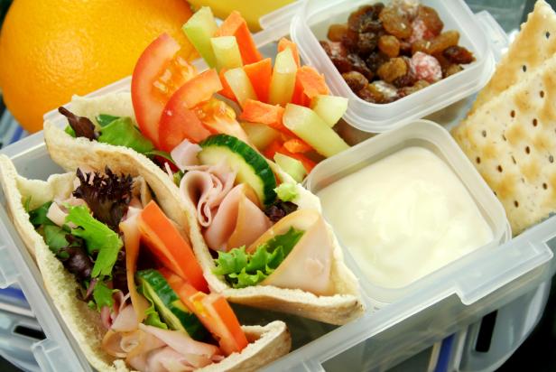 Healthy kid's lunch box made up of pita bread ham and salad, fresh fruit, sultanas and drinking water.