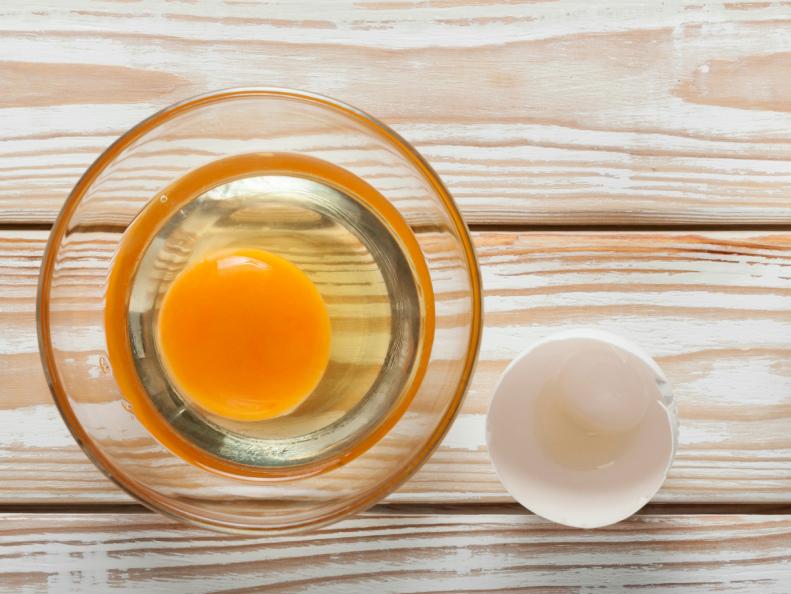 Top view of yolk and egg white in glass bowl on white weathered wooden table