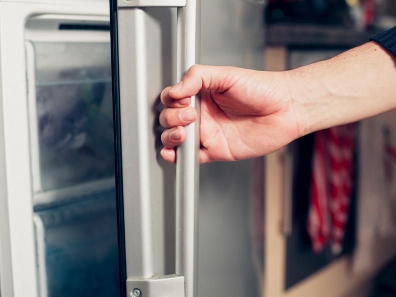 The hand of a young man is opening a freezer door