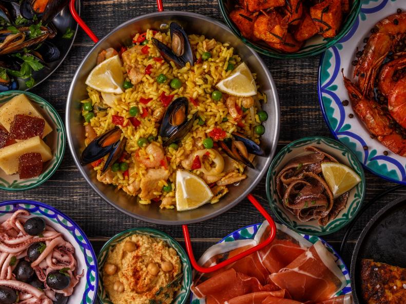 Typical spanish tapas concept. Concept include slices jamon, bowls with olives,  anchovies, spicy potatoes, mashed chickpeas, shrimp, calamari, manchego with quince marmalade, pans with tortilla, paella, mussels  on a wooden table.