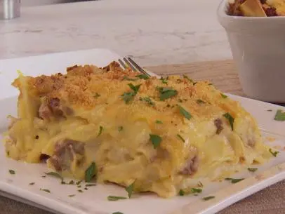 Pasta Pierogi Lasagna was prepared by Chef Stuart O'keeffe. He begins with leftover mashed potatoes that he has heated up. He then adds 1 lb. of ground beef and 8 oz. of italian sausage to a pan and begins to cook them together. While Food and Lifestyle Expert Brandi Milloy cooks the meat of the stove, Chef Stuart O'keeffe makes a roux by melting butter in a warm pan. Once it starts to melt, add and whisk together 4 tablespoons of flour and 4 tablespoons of butter. After it has combined, add in warm milk, stirring as you pour. Whisk together until the mixture thickens. Add in sharp cheddar cheese and mix, seasoning with salt and pepper. Pour a layer of the roux on the bottom of the casserole pan. Next add noodles on top of the roux layer. Food and Lifestyle Expert Brandi finished cooking the meat, removed it, and began to cook the cabbage in the pot. She then added the meat back into the cabbage and combined. Layer the meat and cabbage layer on top of the noodles, then mashed potatoes, then the cheese roux, and repeat. Finish with parmesan cheese and cook for 30-40 minutes on 375 degrees, or until golden brown. Remove, cut, and serve, as seen on Let's Eat, Season 1.
