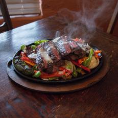 Fajitas served on a sizzling platter topped with peppers, onions and jalapeños at Ninfa's, as seen on Comfort Food Tour, Season 2.