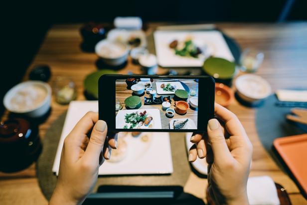 Woman's hand taking a picture of delicate Japanese style cuisine with various side dishes, miso soup and main dishes with smartphone