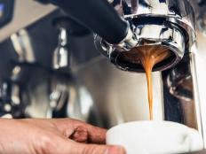 Close up of coffee being brewed by the machine flowing through portafilter into the cup at cafe