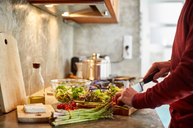 687690097 Midsection of man cutting vegetables. Cropped image of male is preparing food. He is working in kitchen.