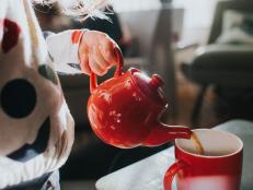 Shiny small red ceramic teapot, pouring hot tea into a red mug. Conceptual with space for copy.