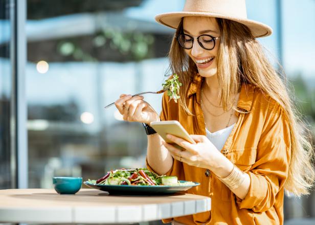 Stylish young woman eating healthy salad on a restaurant terrace, feeling happy on a summer day