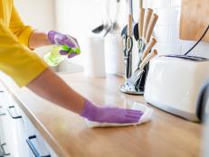 Hands in gloves disinfecting kitchen counter and wiping with paper towel against viruses