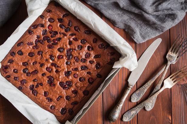 Freshly baked chocolate brownie in square baking tray with paper on rustic wooden background. Dark food photo with shallow focus