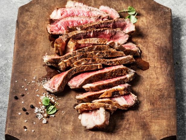 Sliced steak on wooden cutting board on gray background
