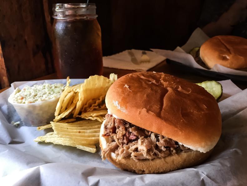 A meal of pulled pork barbeque, potato chips, cole slaw, and sweet tea in a mason jar. A North Carolina southern meal.