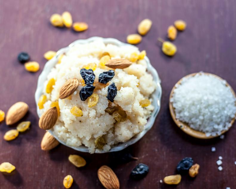 Popular Indian and Asian dessert Suji ka halwa or Rava with organic almonds, cashews and black & golden raisns in a clay bowl on wooden surface. (Popular Indian and Asian dessert Suji ka halwa or Rava with organic almonds, cashews and black & golden r