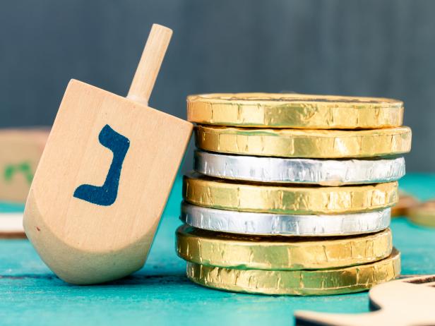 Hanukkah dreidels with some Hanukkah coins and Hanukkah candles on a vintage wood green background. Translation of the hebrew text: Letter N