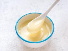 Condensed milk pouring in white bowl. Sweet vanilla sauce, condensed or evaporated milk, top view, copy space.