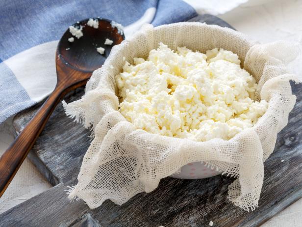 Homemade fresh cottage cheese in gauze and a bowl on the table with linen.