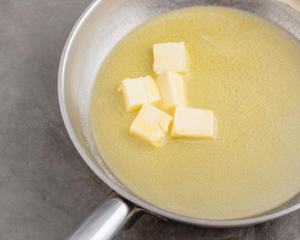 Melting chopped churning butter in silver skillet pan. Butter browning prep step. Greyish surface. High point of view.