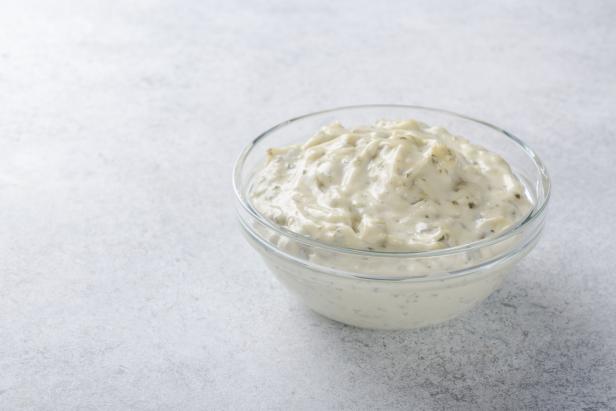 Homemade white sauce tartar tartare in a glass bowl on a light stone background. Horizontal image, copy space
