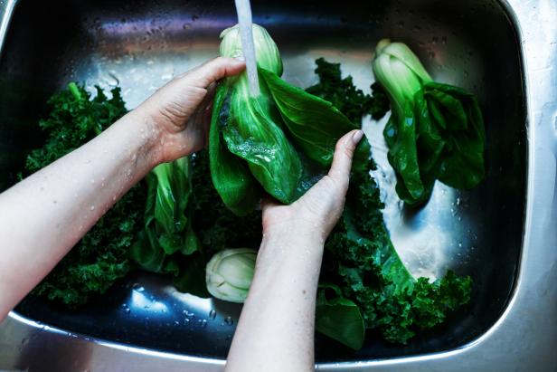 Woman washing in water in sink green chok poy leaves in kitchen, organic healthy food, dark mood image