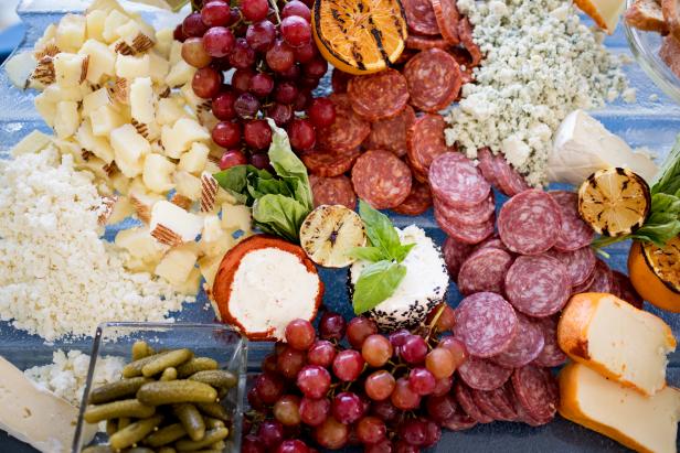 A high angle view of a charcuterie board with cured meats and a variety of cheeses with fruits and basil leaves.