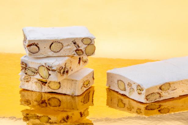 Nougat with almonds and hazelnuts on a golden background where it is reflected, copy space