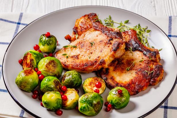 close-up of  fried pork chops with roasted Brussels sprouts sprinkled with fresh red bilberry and thyme on plate
