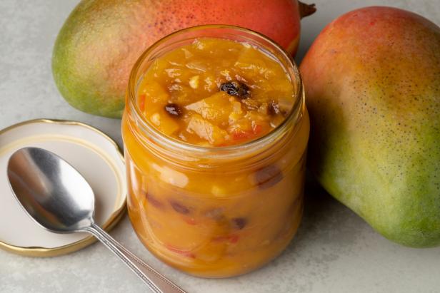 Glass jar with homemade mango chutney and fresh mango close up