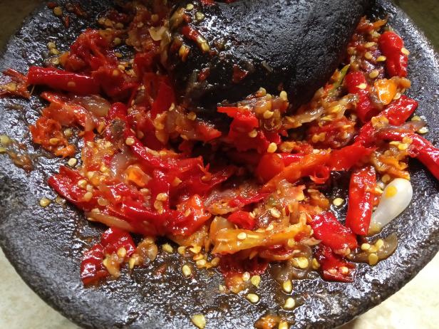 The process of making chili sauce from red chili with a traditional handmade mortar. Indonesian cooking. homemade food. top view