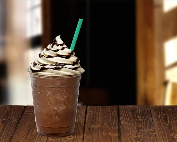 Frappuccino in takeaway cup on wooden table isolated on blackFrappuccino in takeaway cup on wooden table isolated on black