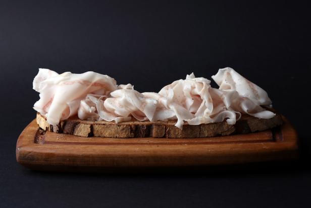 Sandwich with thin slices of salted lard on a wooden board, selective focus. Black background