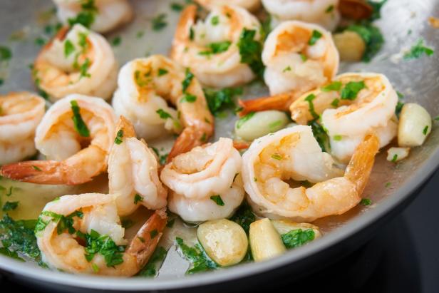 Hand mixing shrimp food with parsley on pan. Keto meal fried prawn for ketogenic diet, preparing sauce for pasta, seafood prawn sizzling in metal frying pan, hot pan-fried paleo food with crispy crust of food rich in cholesterol
