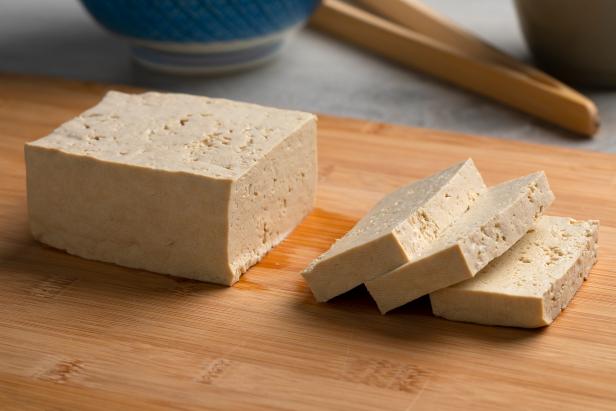 Piece of fresh raw organic tofu and slices on a cutting board close up